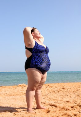 Overweight woman on beach with hands up clipart