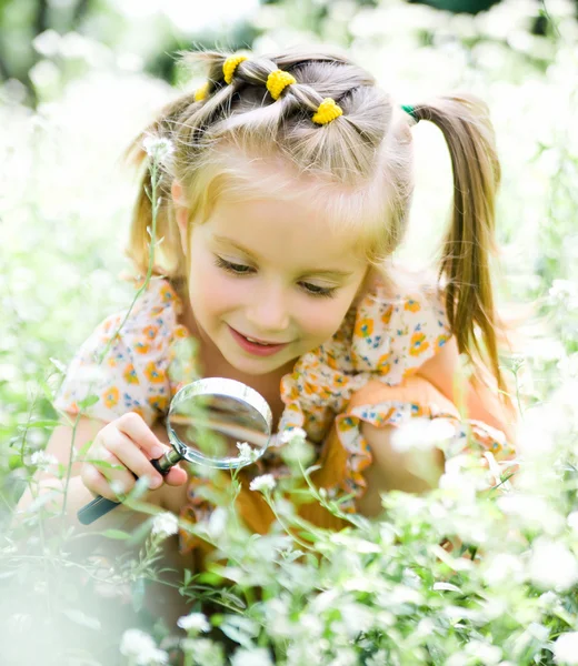 Little girl with magnifying glass looks at flower — Stock Photo, Image