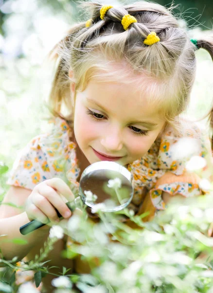 Маленька дівчинка зі збільшувальним склом дивиться на квітку — стокове фото