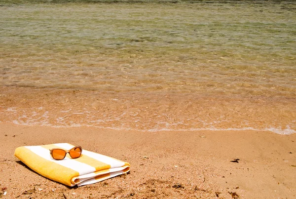 Sunglasses and towel next to the sea. — Stock Photo, Image