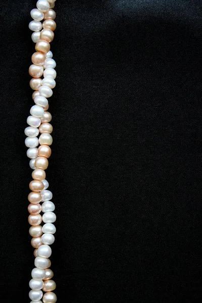 White and pink pearls on the black silk background — Stock Photo, Image