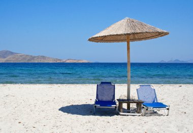 Greece. Kos island. Two chairs and umbrella on the beach clipart