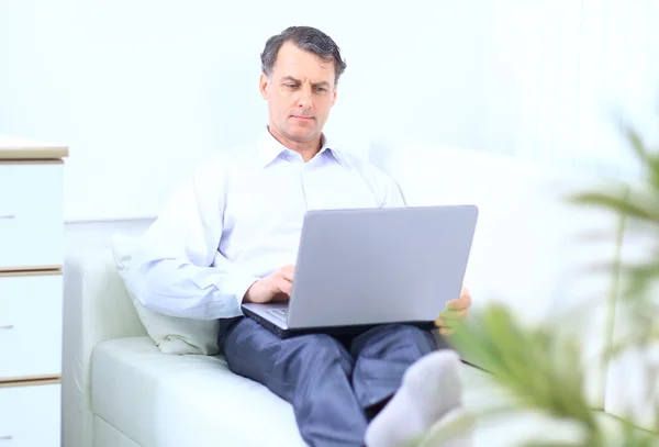 Idősebb férfi a kanapén laptoppal — Stock Fotó