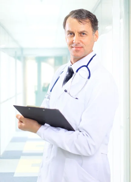 Happy smiling mature doctor writing on clipboard in a modern hospital Stock Photo