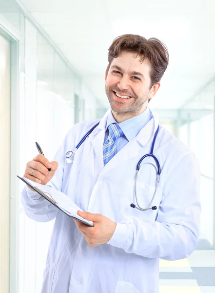 Feliz sonriente médico maduro escribiendo en el portapapeles en un hospital moderno Imágenes de stock libres de derechos