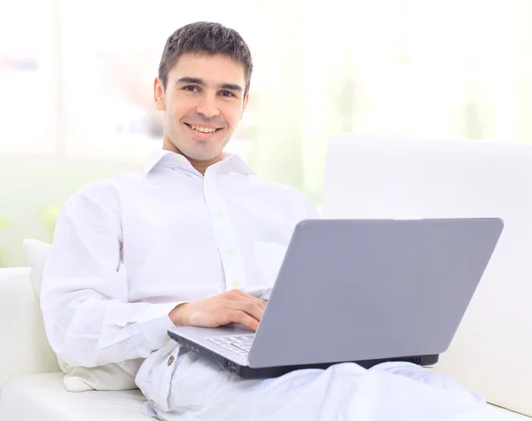 Szczęśliwy młody człowiek siedzi na kanapie z laptopem — Zdjęcie stockowe