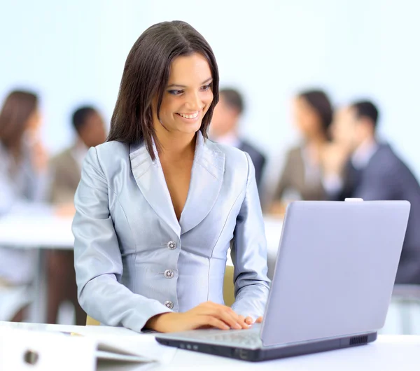 Молодая деловая женщина, работающая за ноутбуком в офисе, улыбается — стоковое фото