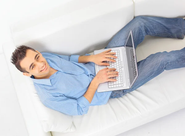 Bir dizüstü bilgisayar kullanırken kanepede rahatlatıcı bir adam portresi — Stok fotoğraf