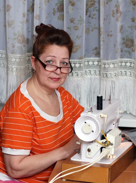 Old woman sews clothes in-home — Stock Photo, Image