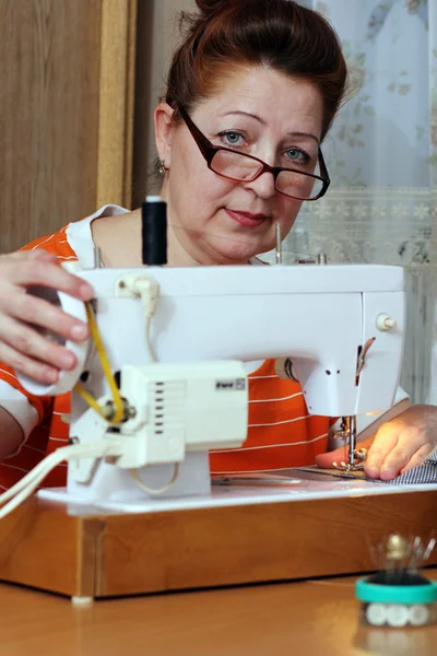 Old woman sews clothes in-home — Stock Photo, Image