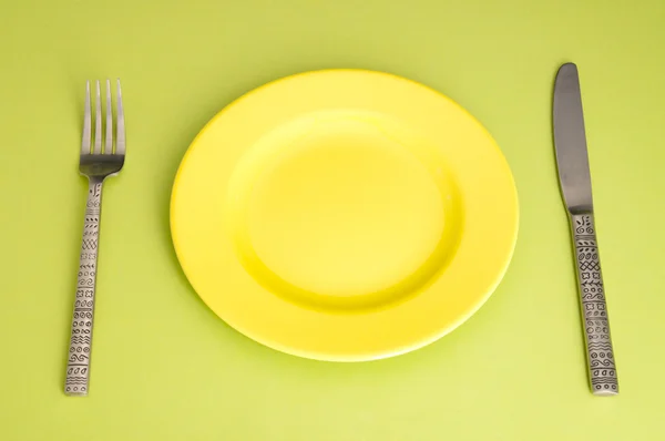 Cuchillo, placa amarilla y tenedor sobre fondo verde — Foto de Stock