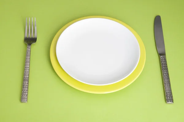 Cuchillo, platos y tenedor sobre fondo verde — Foto de Stock