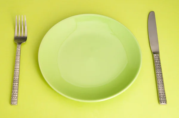 Knife, green plate and fork on yellow background — Stock Photo, Image