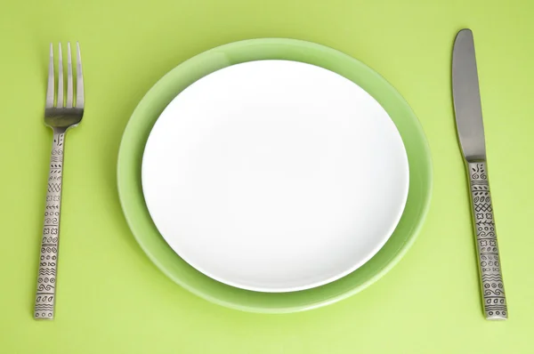Coltello, piastre e forchetta su sfondo verde — Foto Stock
