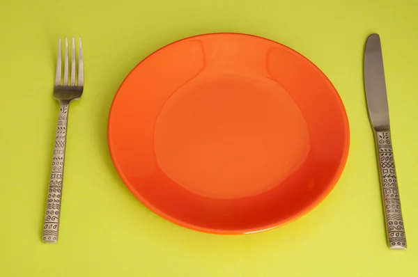 Knife, red plate and fork on green background — Stock Photo, Image