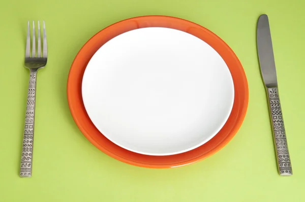 Faca, pratos e garfo sobre fundo verde — Fotografia de Stock