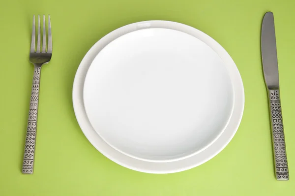 Cuchillo, plato blanco y tenedor sobre fondo verde — Foto de Stock