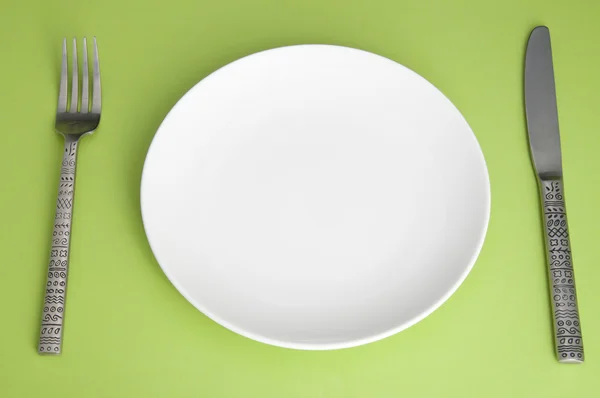 Нож, белая тарелка и вилка на зеленом фоне — стоковое фото