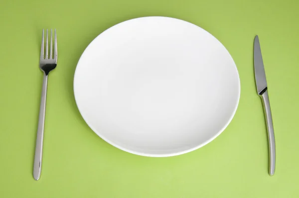 Knife, white plate and fork on green background — Stock Photo, Image