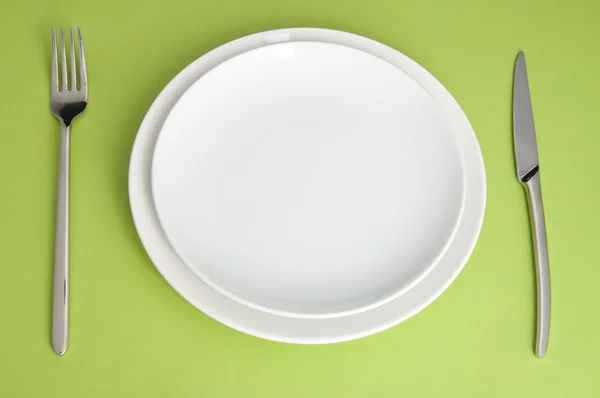 Faca, placa branca e garfo no fundo verde — Fotografia de Stock