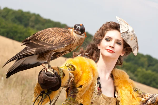 Kvinnan i en vacker gammal stil klänning med falcon har en vila — Stockfoto