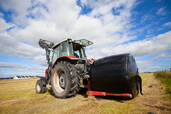 Tracteur ramassant un rouleau de meule de foin sur le terrain — Photo