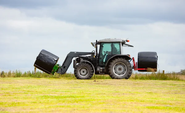 Traktor sběr roll sena v poli — Stock fotografie