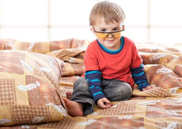 En pojke i roliga glasögon på sängen — Stockfoto