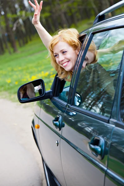 Una mujer sonriente en un coche está meneando —  Fotos de Stock
