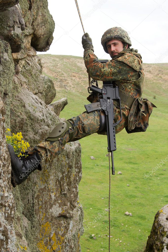 Armed military alpinist hanging on rope