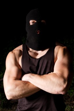 Pumped thug in black mask outdoors at night clipart