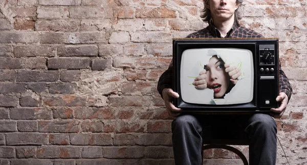 TV com uma foto da menina virada através de um buraco nas mãos de um assento — Fotografia de Stock