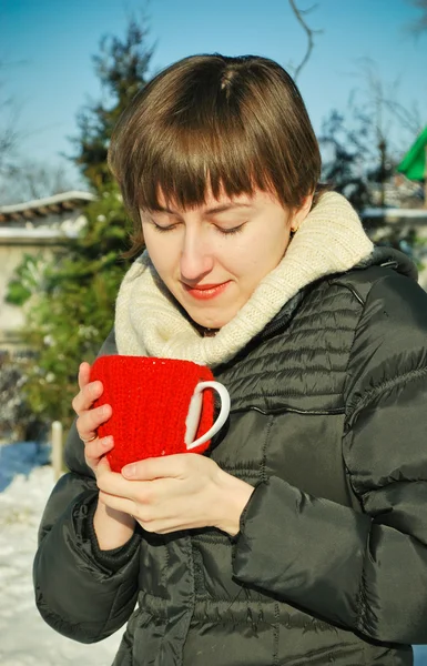 Jonge vrouw drinken van hete thee buitenshuis in ondergesneeuwd binnentuintje — Stockfoto