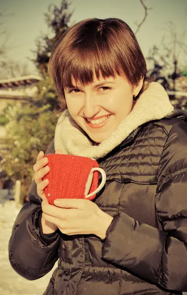 Jonge vrouw drinken van hete thee buitenshuis in ondergesneeuwd binnentuintje — Stockfoto