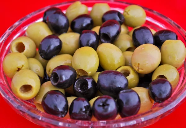Black and green olives in a crystal bowl isolated on red — Stock Photo, Image
