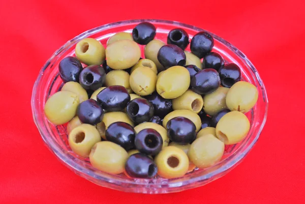 Black and green olives in a crystal bowl isolated on red — Stock Photo, Image