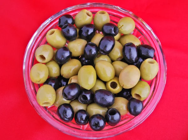 Olives noires et vertes dans un bol en cristal isolé sur rouge — Photo
