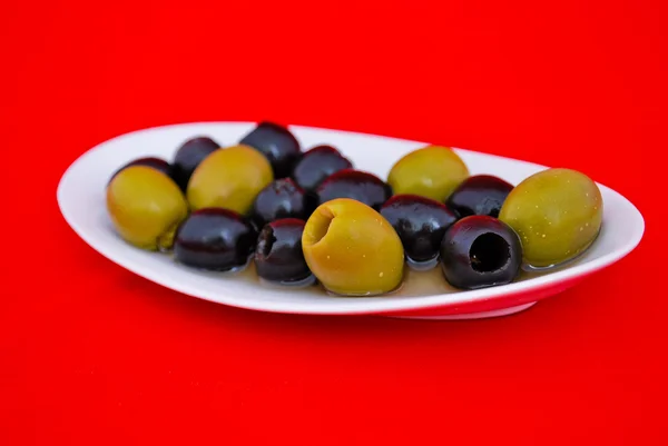 Olives noires et vertes dans une assiette sur fond rouge — Photo