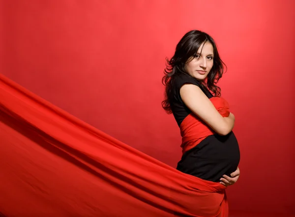 Беременная в черном платье и красной одежде на красном — стоковое фото