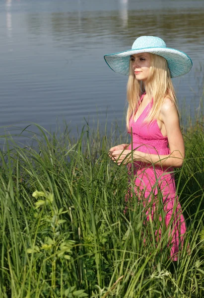 Krásná blondýna v klobouku na břehu řeky. — Stock fotografie