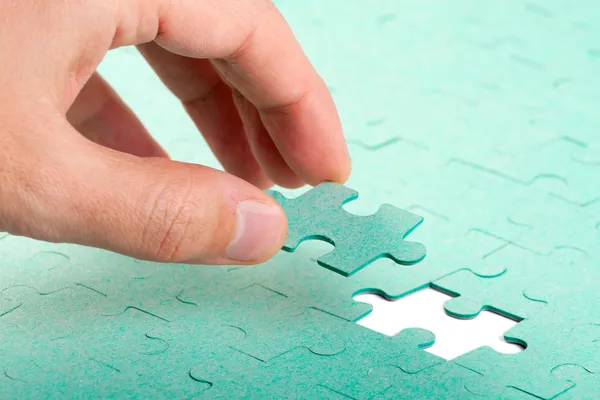 Hand inserting missing piece of green jigsaw puzzle into the hol — Stock Photo, Image