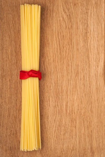 Bunch of spaghetti tied up with a red ribbon on wooden backgroun — Stock Photo, Image