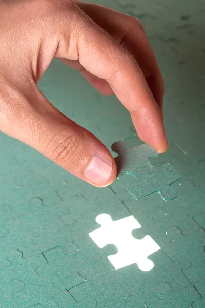 Hand inserting missing piece of green jigsaw puzzle into the hol — Stock Photo, Image