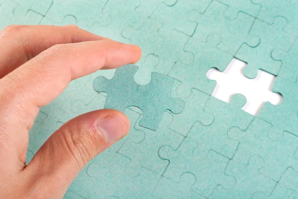 Hand inserting missing piece of green jigsaw puzzle into the hol Stock Photo