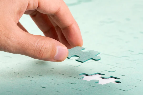 Hand inserting missing piece of green jigsaw puzzle into the hol Stock Picture