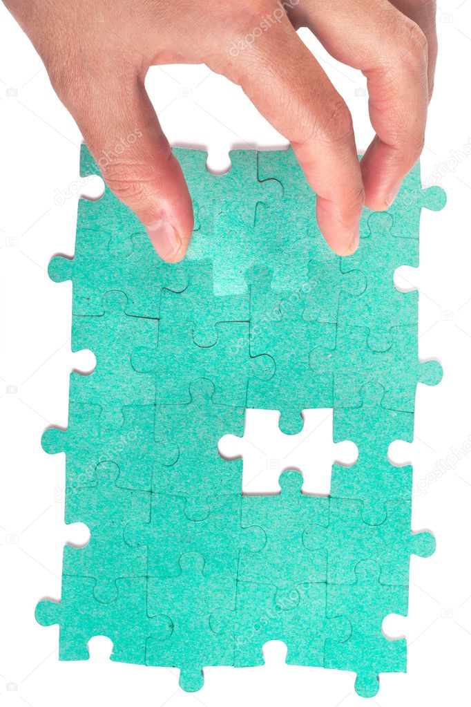 Hand inserting missing piece of green jigsaw puzzle into the hol