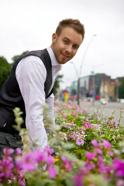 Jonge aantrekkelijke man tegen bedden met mooie bloemen. — Stockfoto