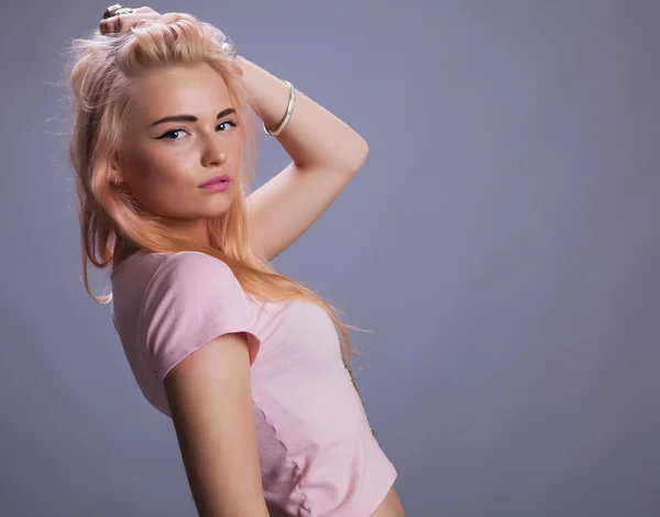 Блондинка в розовом на сером фоне студии — стоковое фото