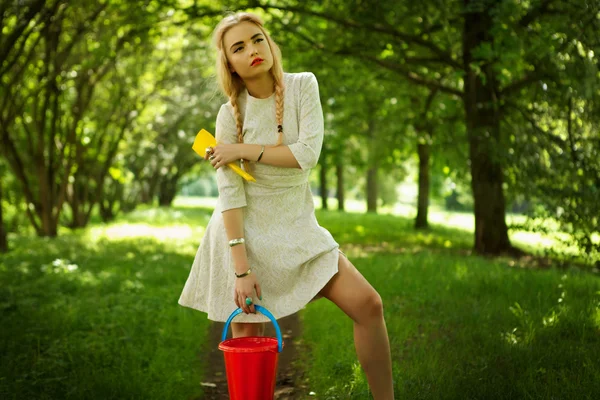 La giovane bionda alla moda posa in viale di parco con un secchio rosso . — Foto Stock