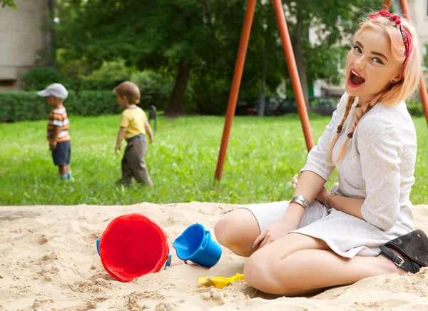 Όμορφη νεαρή κοπέλα κάθεται στο sandbox για παιδιά. — Φωτογραφία Αρχείου